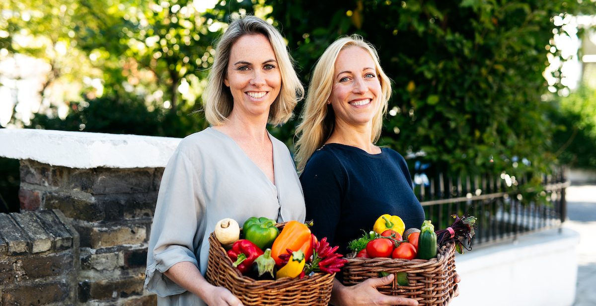 Two women with baskets of colourful vegetables