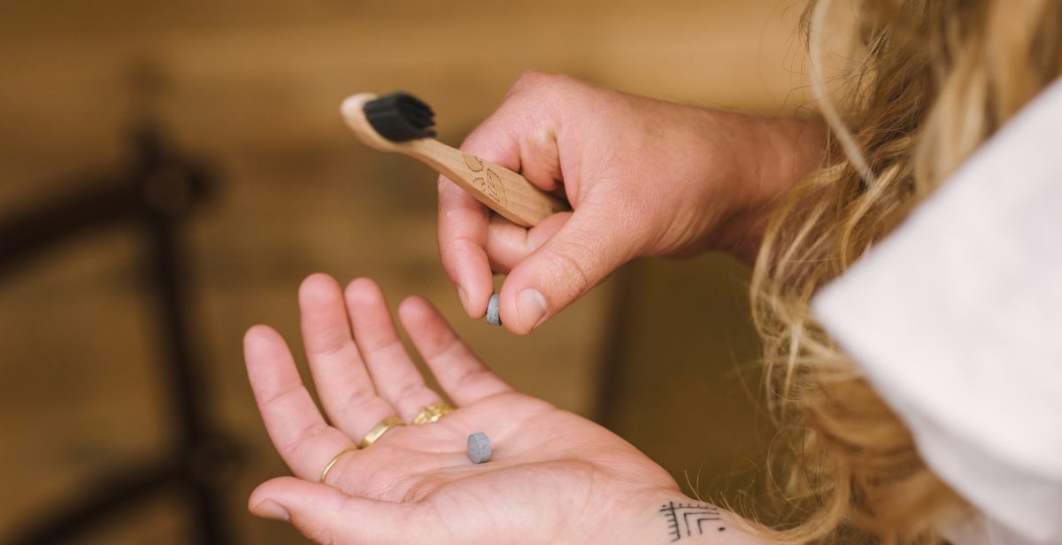 woman's hand holding wooden toothbrush and toothpast tablet