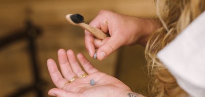woman's hand holding wooden toothbrush and toothpast tablet